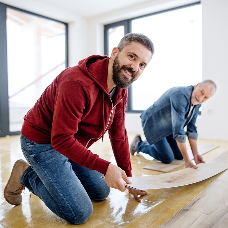A mature man with his senior father laying vinyl flooring, a new home concept.